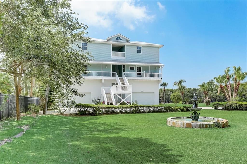 A light blue stilt house with a wraparound porch and a stone fountain in the yard — 2424 BAY DRIVE UNIT 2424/2426, BRADENTON, FL