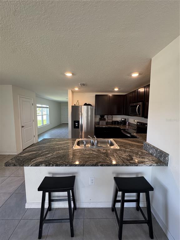 A kitchen features dark wood cabinets, stainless steel appliances, and a granite-topped breakfast bar — 4234 AUTUMN FOG COURT, PALMETTO, FL