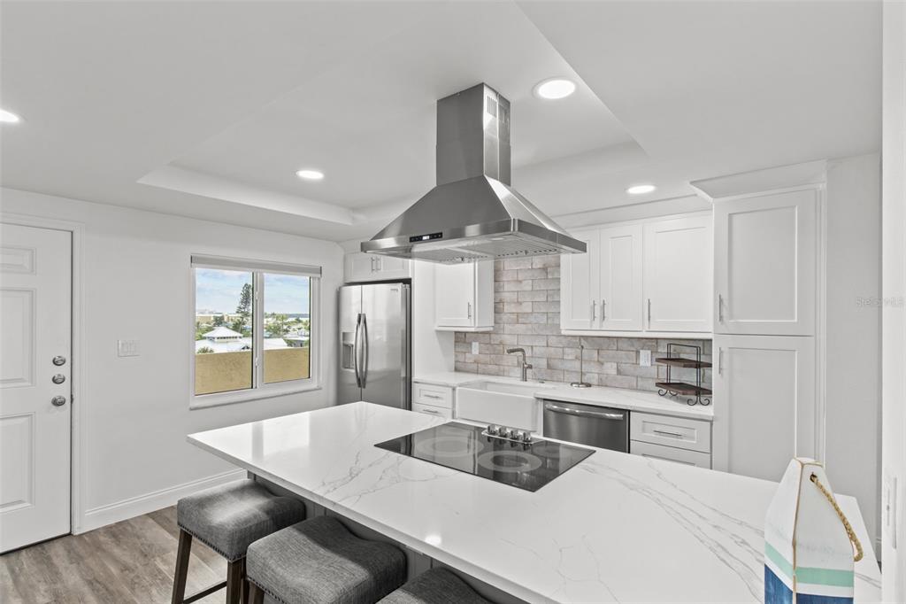 A modern kitchen features white cabinetry, a marble-topped island with a cooktop, and stainless appliances — 14950 GULF BOULEVARD UNIT 503, MADEIRA BEACH, FL