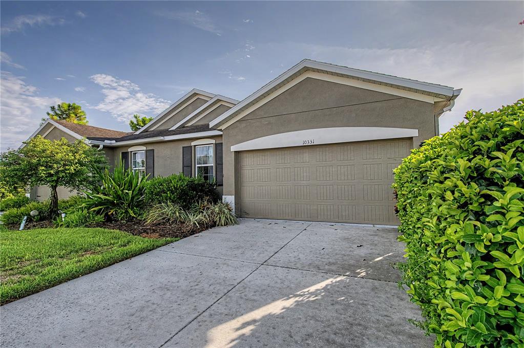 A beige single-story house features a two-car garage, a concrete driveway, and landscaped front yard — 10331 HERON HIDEAWAY LOOP, LAND O LAKES, FL