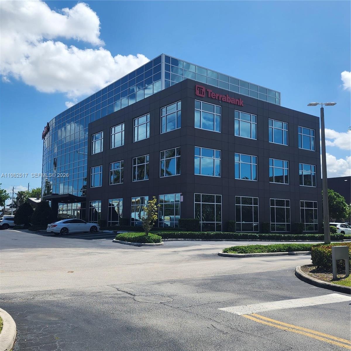 A modern, multi-story office building with a glass facade and dark panels under a blue sky — 2500 NW 107th Ave # 400, Doral FL 33172, DORAL, FL