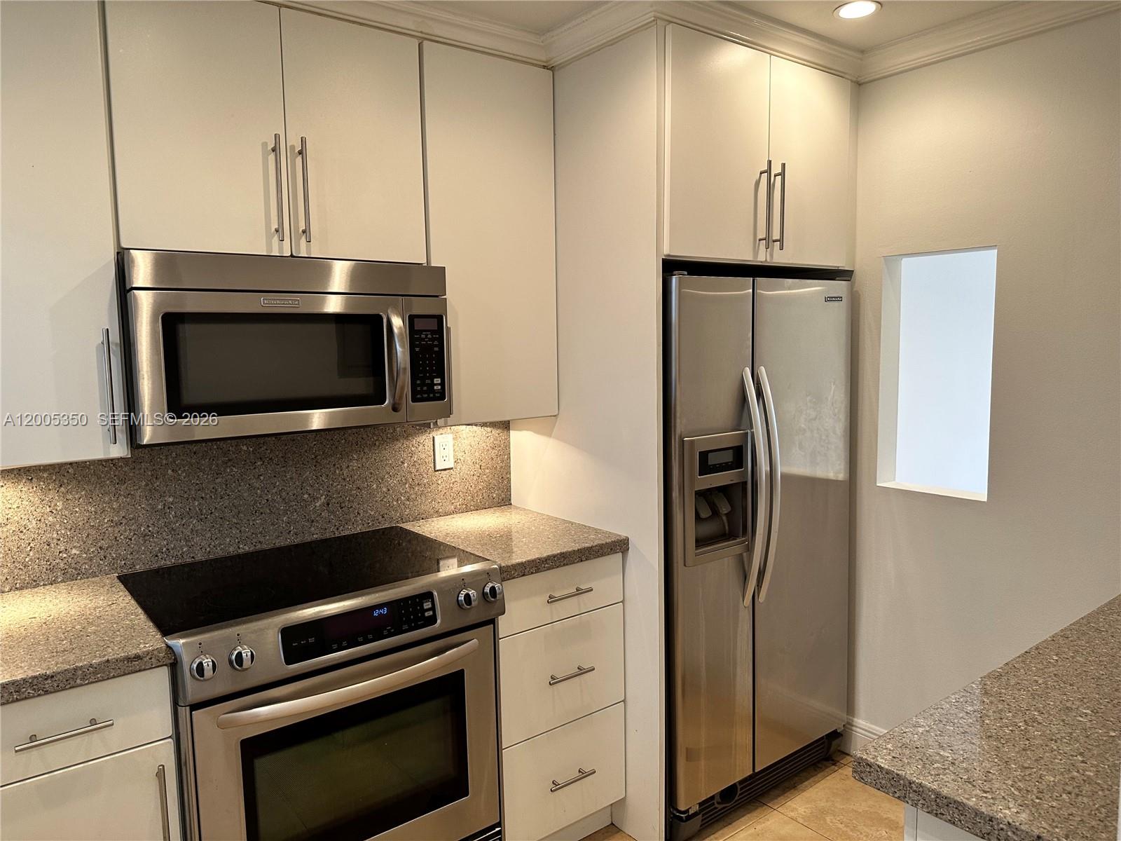 A kitchen features stainless steel appliances, white cabinetry, and speckled granite countertops — 1250 Lincoln Rd # 406, Miami Beach FL 33139, MIAMI BEACH, FL