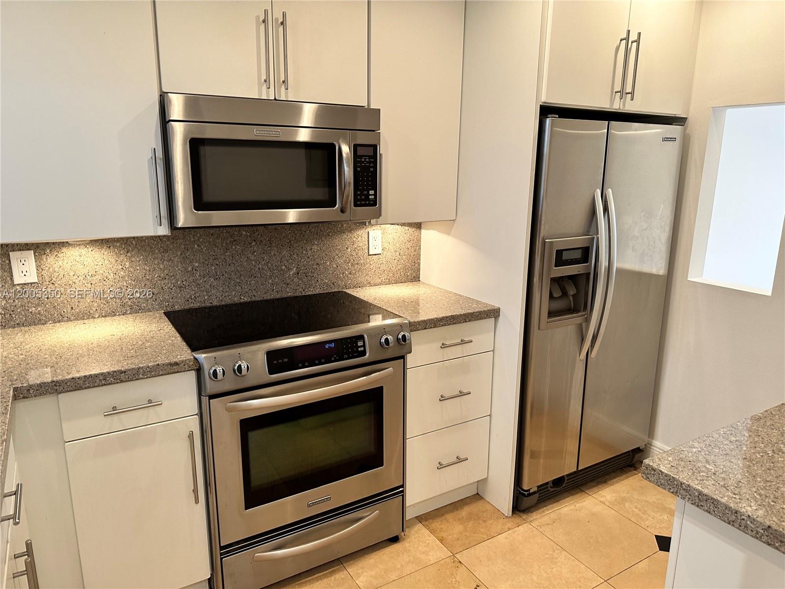 A kitchen features white cabinets, stainless steel appliances, and speckled granite countertops — 1250 Lincoln Rd # 406, Miami Beach FL 33139, MIAMI BEACH, FL