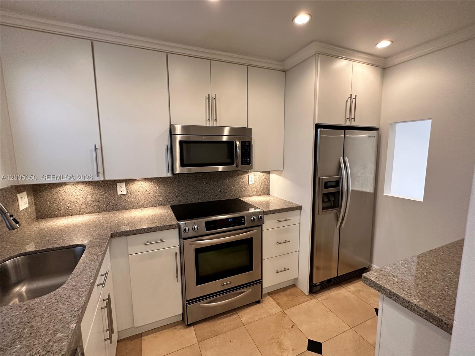 A kitchen features white cabinets, stainless steel appliances, and speckled granite countertops — 1250 Lincoln Rd # 406, Miami Beach FL 33139, MIAMI BEACH, FL