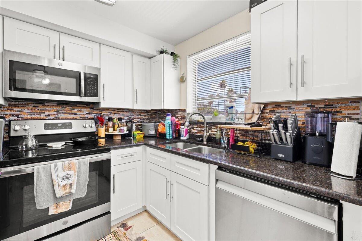 A kitchen features white cabinets, stainless steel appliances, a dark granite countertop, and a tiled backsplash — 1905 Lake Worth Road, FL 33461, FL