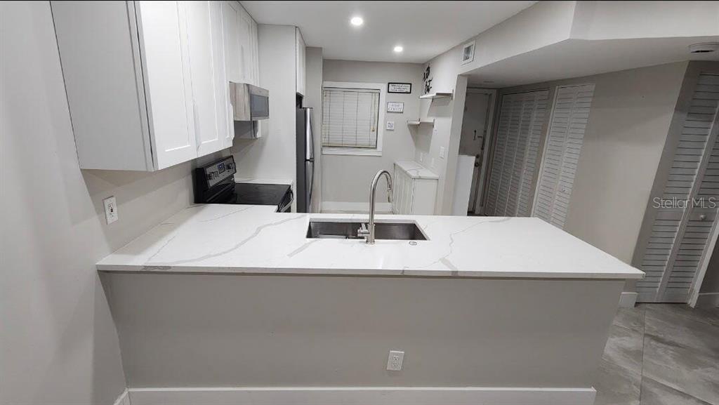 A kitchen with a white quartz peninsula, stainless steel sink, and white cabinetry — 8605 W SAMPLE ROAD UNIT 311, CORAL SPRINGS, FL
