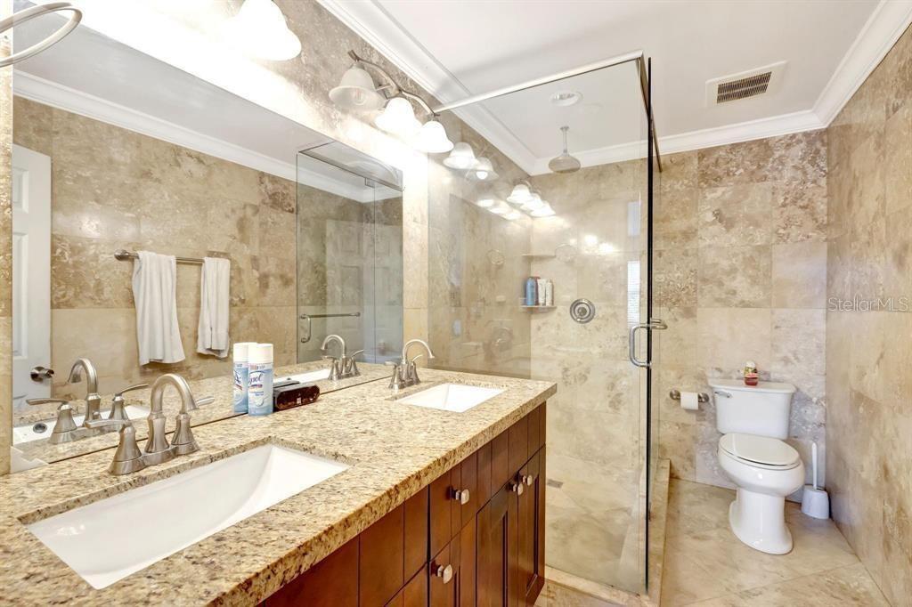 A bathroom features a double vanity with granite countertops, a glass-enclosed shower, and beige tiling — 8605 W SAMPLE ROAD UNIT 311, CORAL SPRINGS, FL