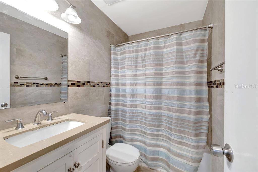 A bathroom features a white vanity, a toilet, and a shower with a striped curtain — 8605 W SAMPLE ROAD UNIT 311, CORAL SPRINGS, FL