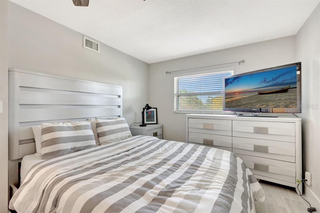 A bedroom features a white paneled headboard, striped bedding, a dresser with a television, and blinds — 8605 W SAMPLE ROAD UNIT 311, CORAL SPRINGS, FL