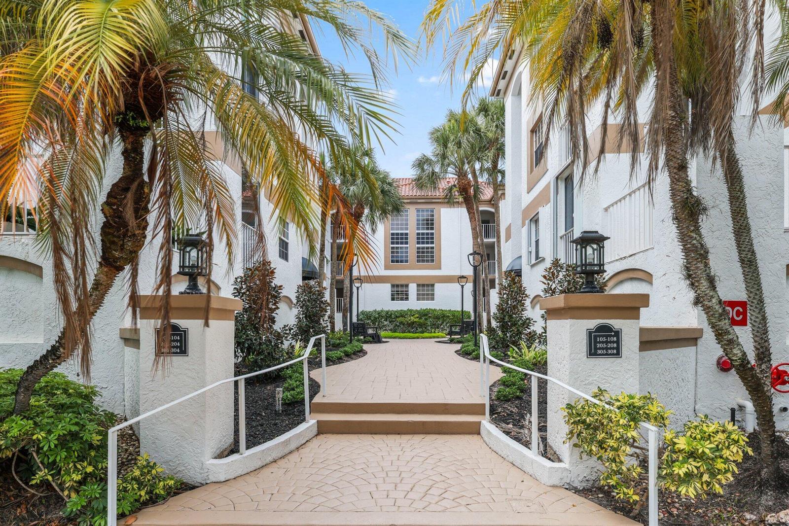 A paved walkway leads between two white apartment buildings with palm trees and landscaping — 7370 Orangewood Lane # 302, Boca Raton FL 33433, BOCA RATON, FL