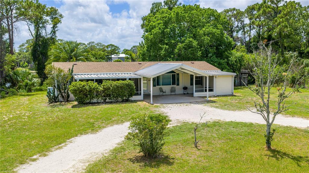 A single-story house with a metal-roofed carport and a screened porch sits on a grassy lot — 1055 ACEE DRIVE, NEW SMYRNA BEACH, FL