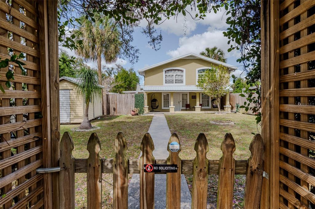 A two-story house with a yellow exterior is viewed through a wooden gate and trellis — 203 W CREST AVENUE, TAMPA, FL
