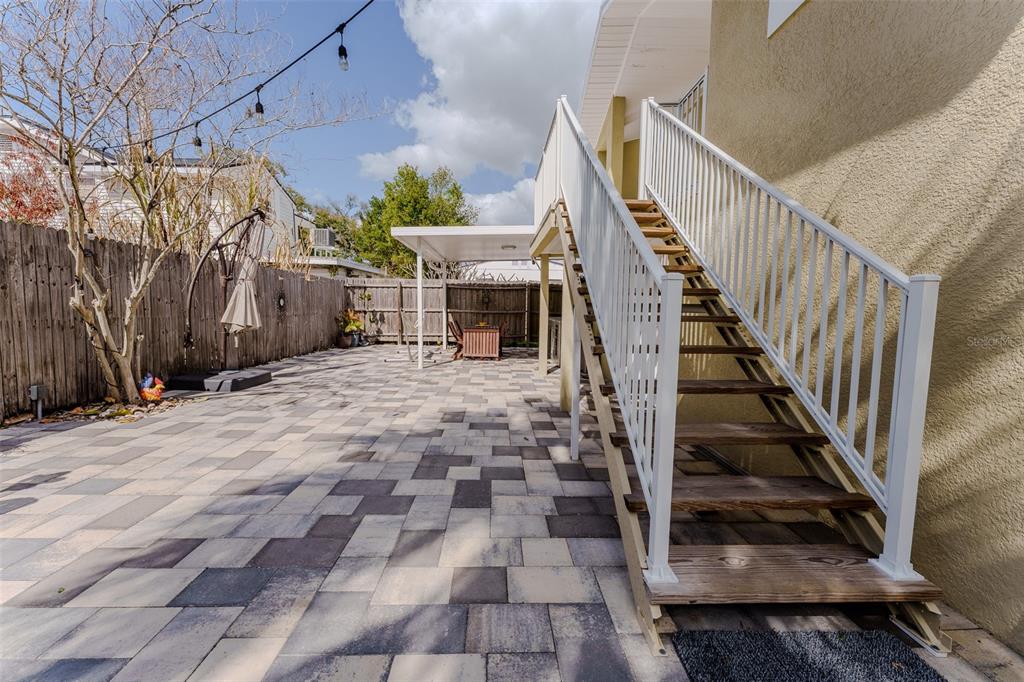 A paved backyard patio features a wooden staircase leading to an elevated deck — 203 W CREST AVENUE, TAMPA, FL