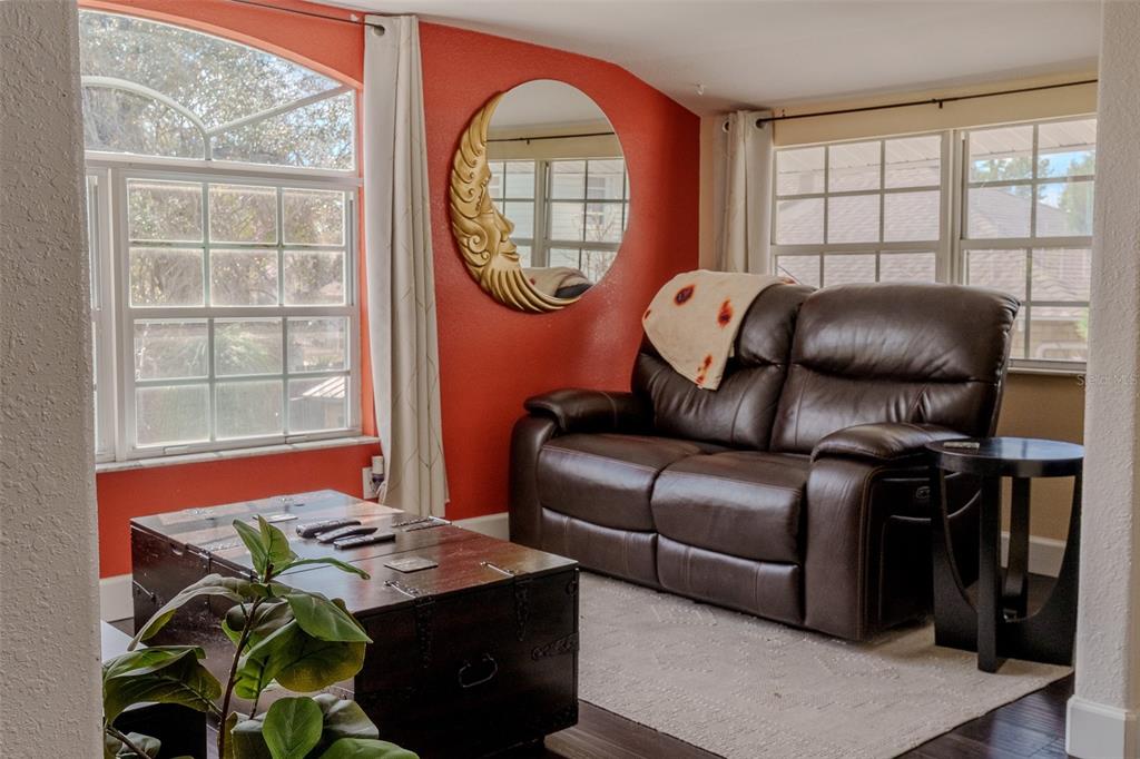 A living room features a brown leather loveseat, a wooden trunk coffee table, and a crescent-moon mirror — 203 W CREST AVENUE, TAMPA, FL