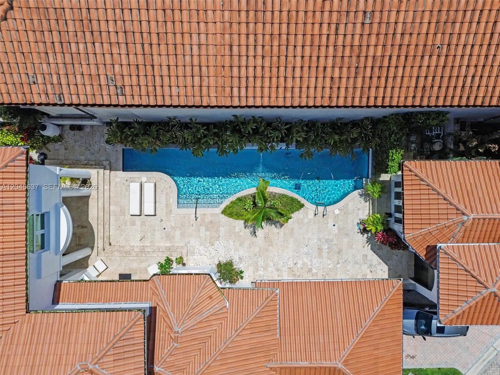 An aerial view shows a swimming pool with a central island in a paved courtyard — 13689 Deering Bay Dr, Coral Gables FL 33158, CORAL GABLES, FL