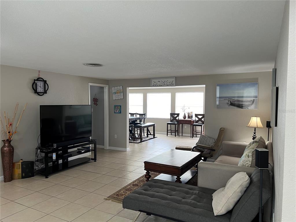 A living room with tile floors, a television, and an adjacent dining area with windows — 705 CRESTVIEW CIRCLE NW, PORT CHARLOTTE, FL