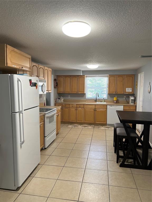 A kitchen features light wood cabinets, white appliances, tile flooring, and a dark dining table — 705 CRESTVIEW CIRCLE NW, PORT CHARLOTTE, FL