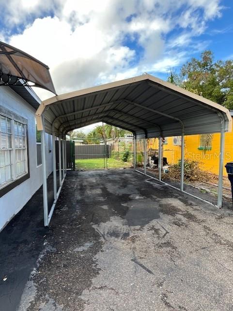A metal carport stands over a paved driveway next to a house with a yellow wall — 6708 N ARMENIA AVENUE, TAMPA, FL
