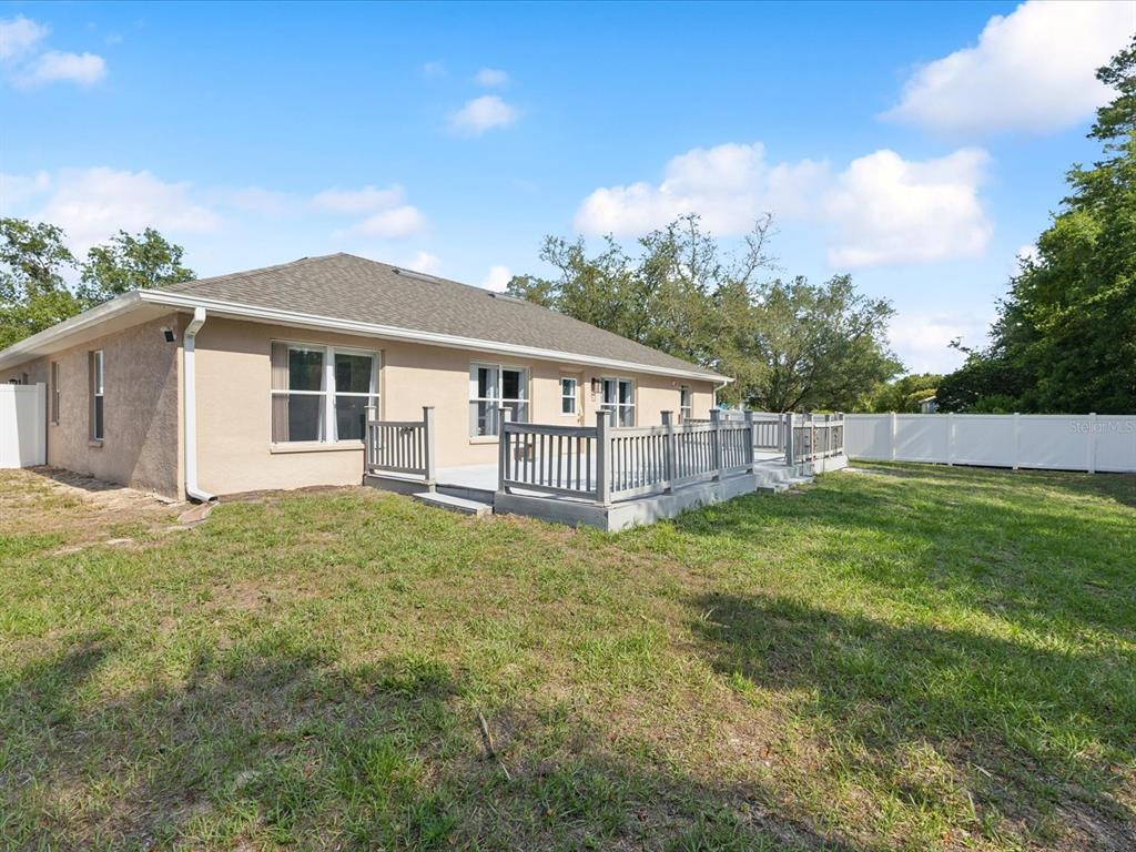 The rear exterior of a tan house features a gray wooden deck and white fencing — 6076 SHIPROCK AVENUE, SPRING HILL, FL