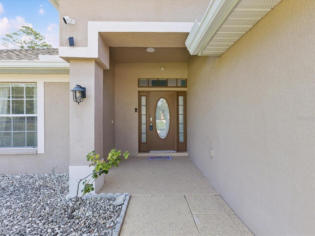 A tan stucco house exterior features a front door with a glass oval insert — 6076 SHIPROCK AVENUE, SPRING HILL, FL