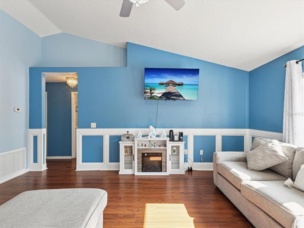 A living room features blue walls with white wainscoting, a wall-mounted television, and a fireplace — 6076 SHIPROCK AVENUE, SPRING HILL, FL
