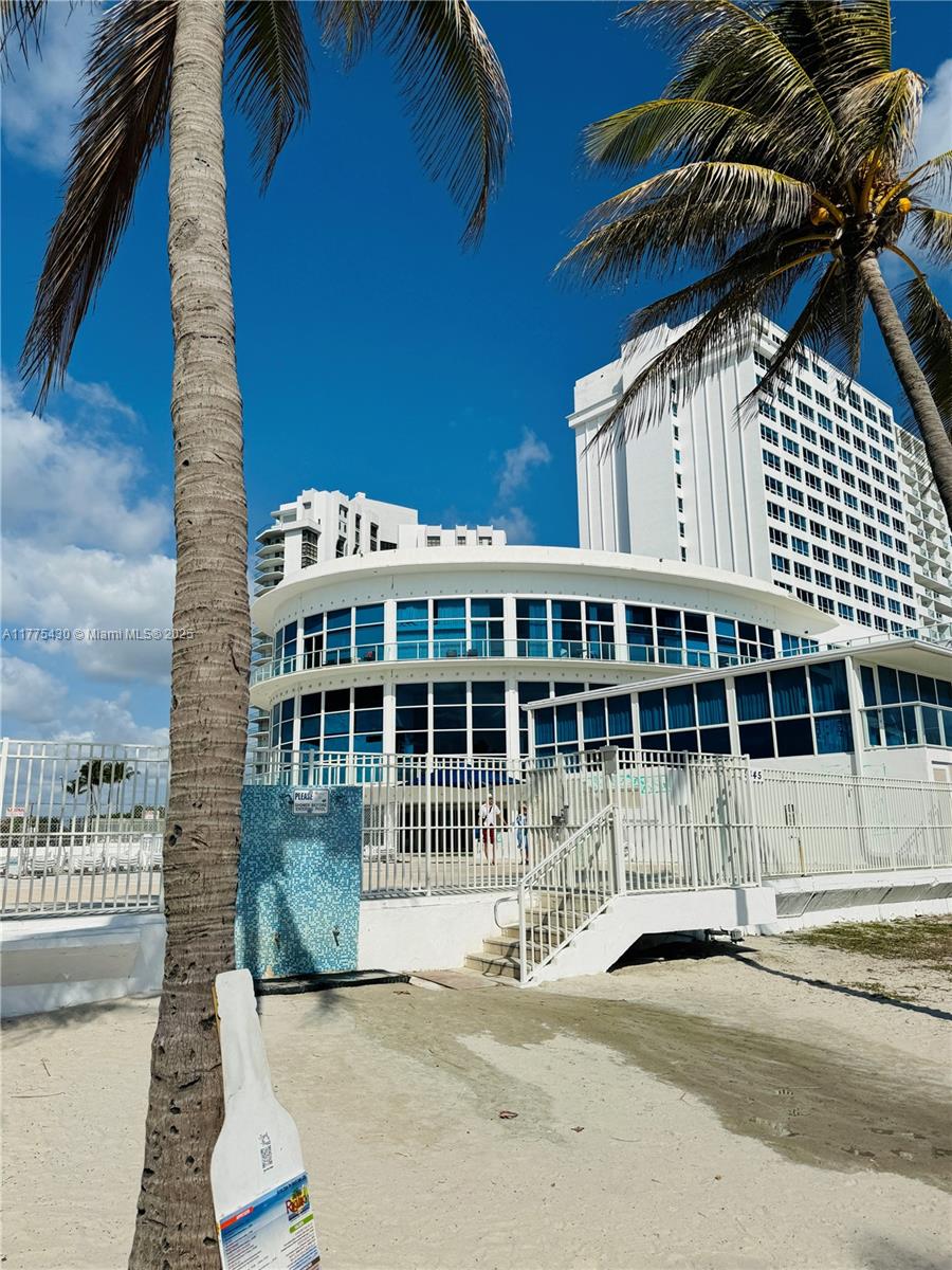 A white multi-story building with a curved glass facade stands behind a beachside fence — 5445 Collins Ave # 1520, Miami Beach FL 33140, MIAMI BEACH, FL
