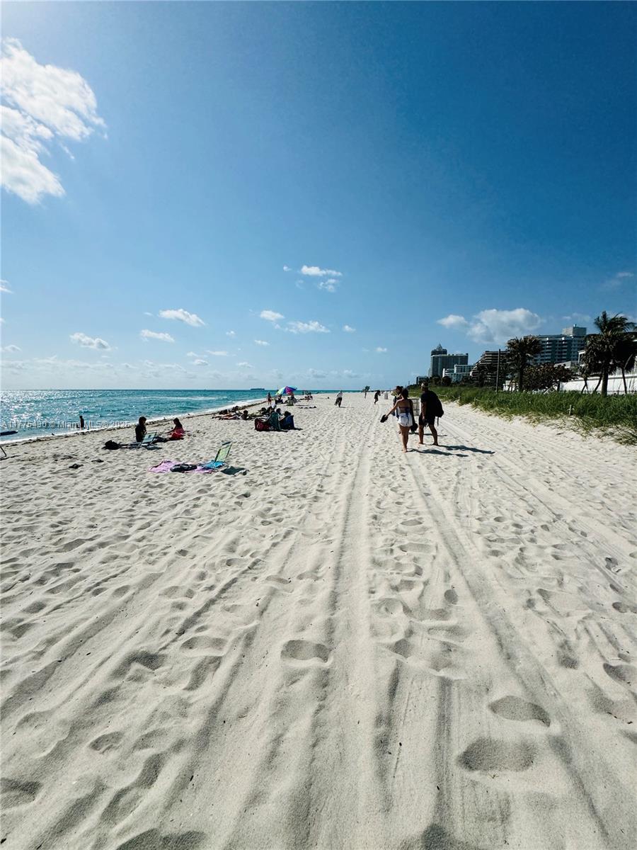 A wide, sandy beach with tire tracks, people walking, and distant buildings under a blue sky — 5445 Collins Ave # 1520, Miami Beach FL 33140, MIAMI BEACH, FL