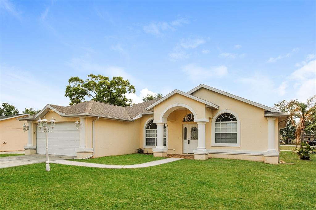 A single-story, light yellow stucco house with a two-car garage and arched entryway — 3428 TOMAHAWK AVENUE, SPRING HILL, FL