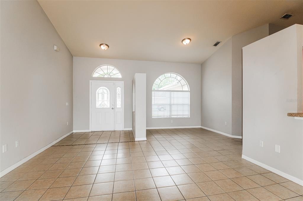 An empty room with beige tile flooring, light gray walls, and arched windows — 3428 TOMAHAWK AVENUE, SPRING HILL, FL