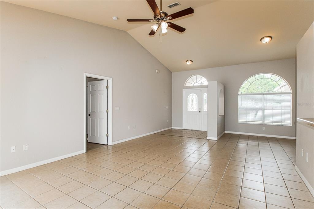 A spacious living room features vaulted ceilings, tile flooring, a ceiling fan, and arched windows — 3428 TOMAHAWK AVENUE, SPRING HILL, FL