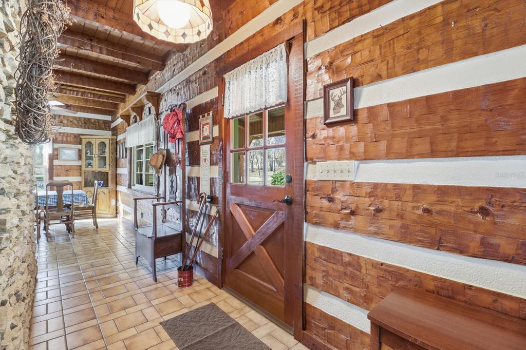 A rustic entryway features log walls, tile flooring, and a wooden door with glass panels — 7310 S IRMA POINT, LECANTO, FL