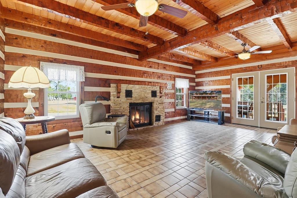 A rustic living room features log walls, exposed ceiling beams, a stone fireplace, and tile flooring — 7310 S IRMA POINT, LECANTO, FL