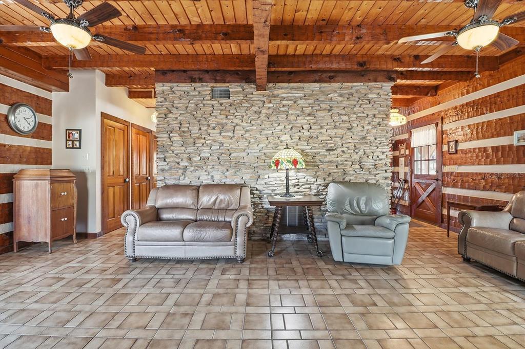 A rustic living room features a stone accent wall, wood-beamed ceiling, and tiled flooring — 7310 S IRMA POINT, LECANTO, FL