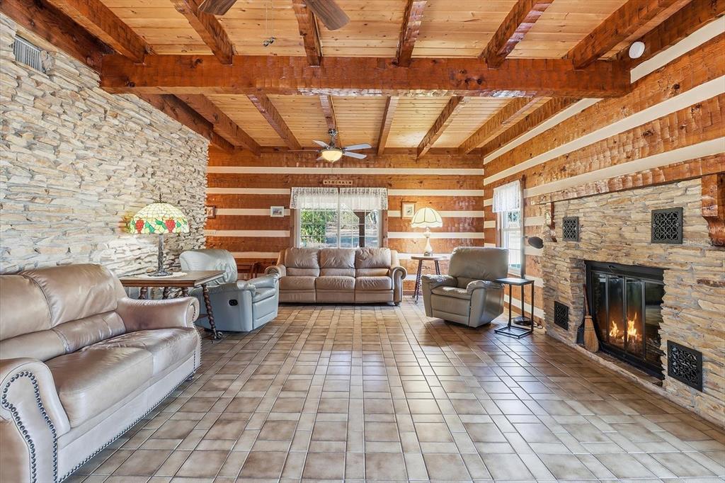A rustic living room features log walls, a stone fireplace, and exposed wooden ceiling beams — 7310 S IRMA POINT, LECANTO, FL
