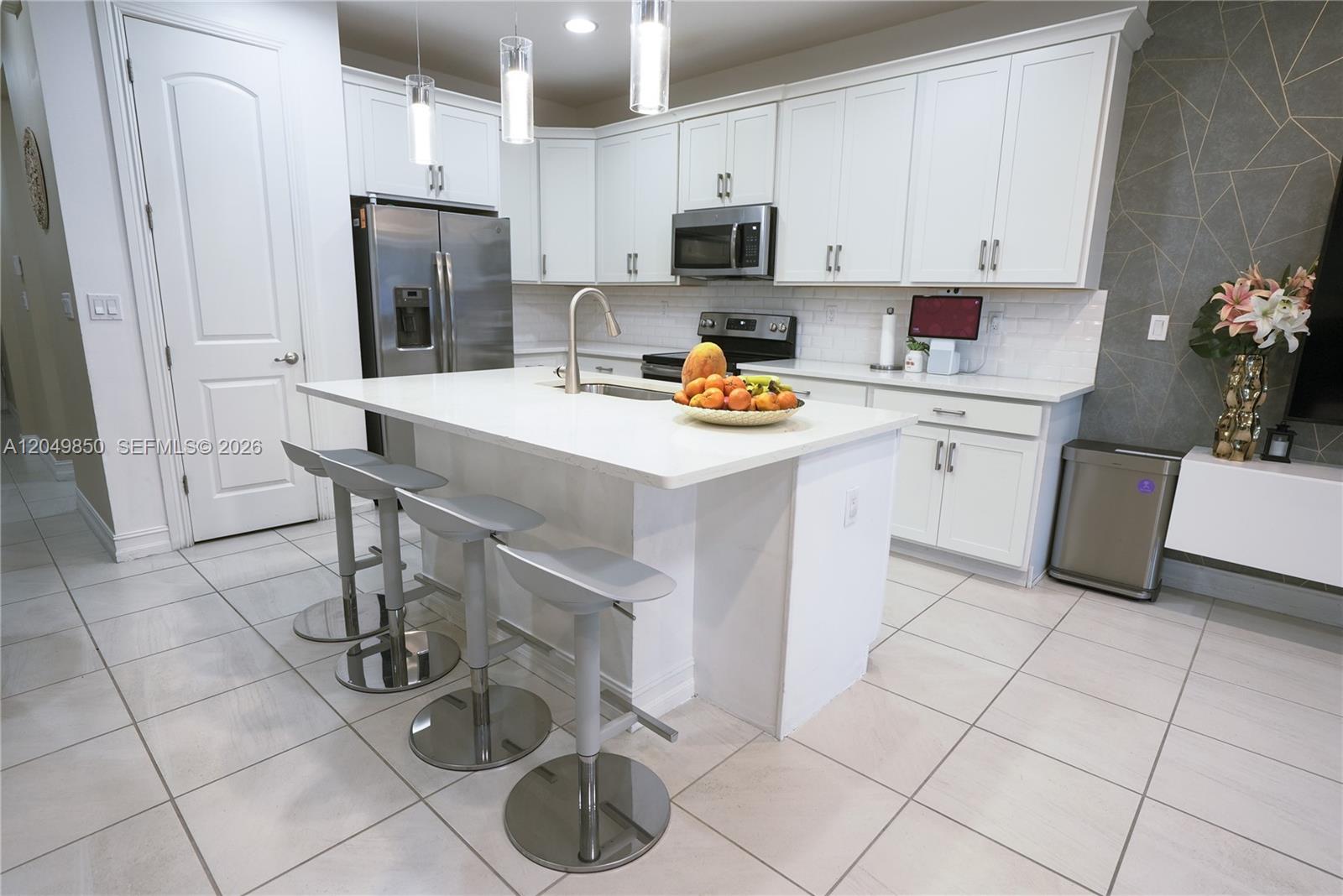 A modern kitchen features white cabinetry, a central island with bar seating, and tile flooring — 10111 Akenside Dr, Boca Raton FL 33428, BOCA RATON, FL