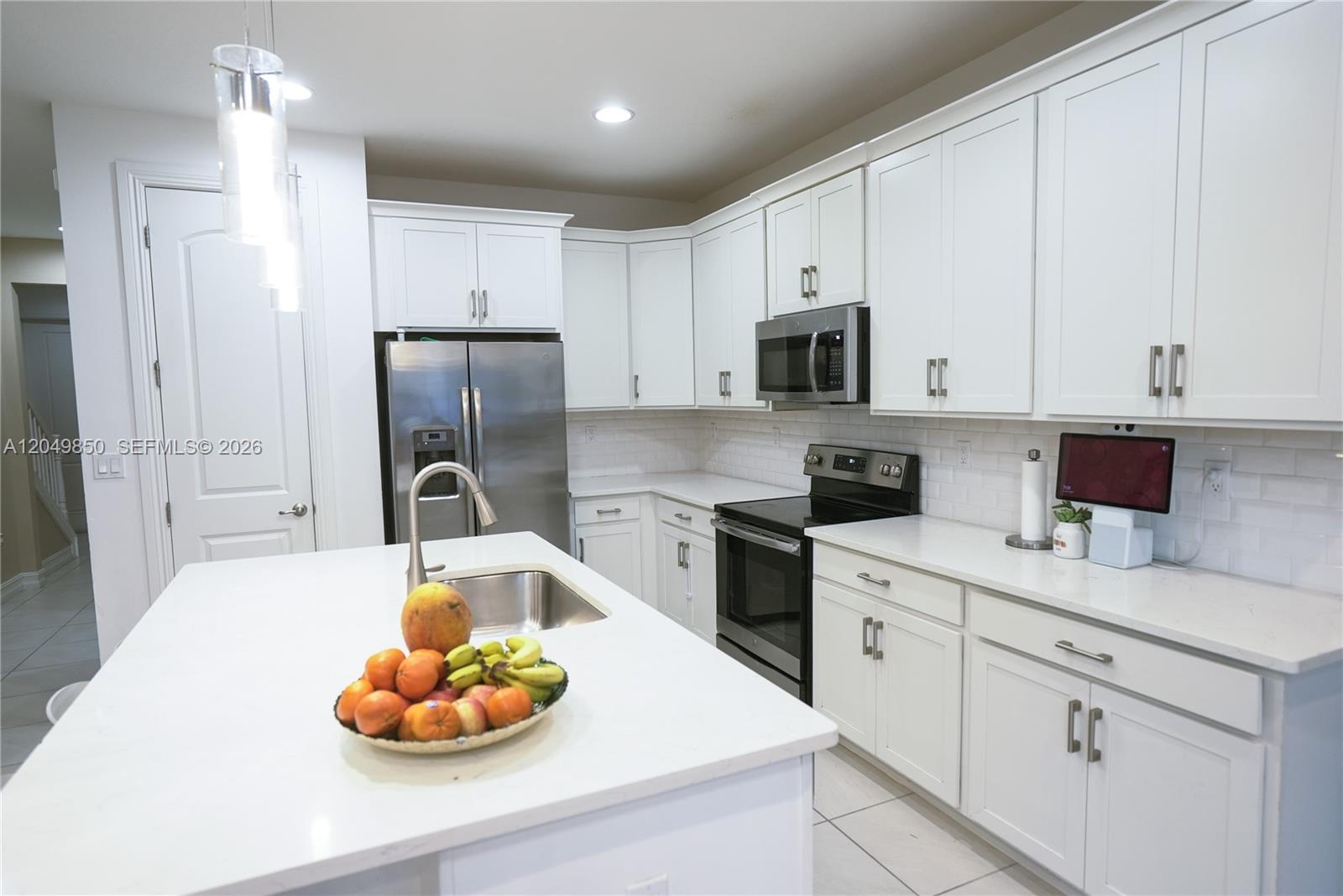 A kitchen features white cabinets, stainless steel appliances, a center island, and a subway tile backsplash — 10111 Akenside Dr, Boca Raton FL 33428, BOCA RATON, FL