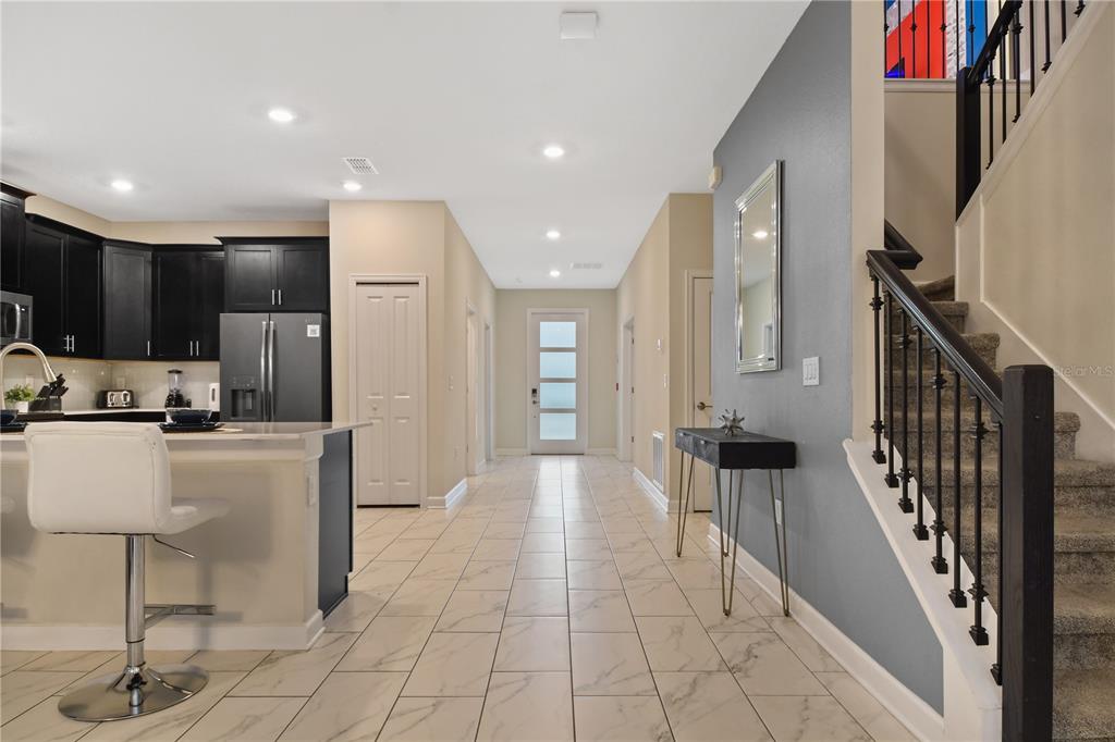 A kitchen with dark cabinets and a breakfast bar overlooks a tiled hallway and staircase — 4547 NARRATIVE LANE, KISSIMMEE, FL