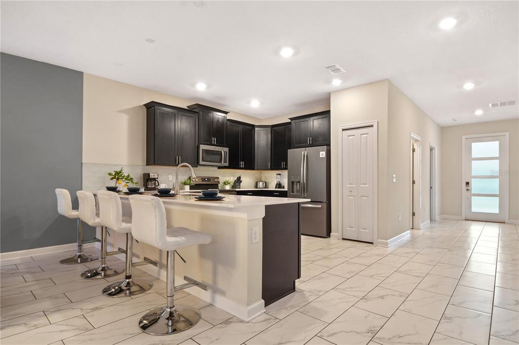 A kitchen features dark cabinets, a white quartz island with bar stools, and tiled floors — 4547 NARRATIVE LANE, KISSIMMEE, FL