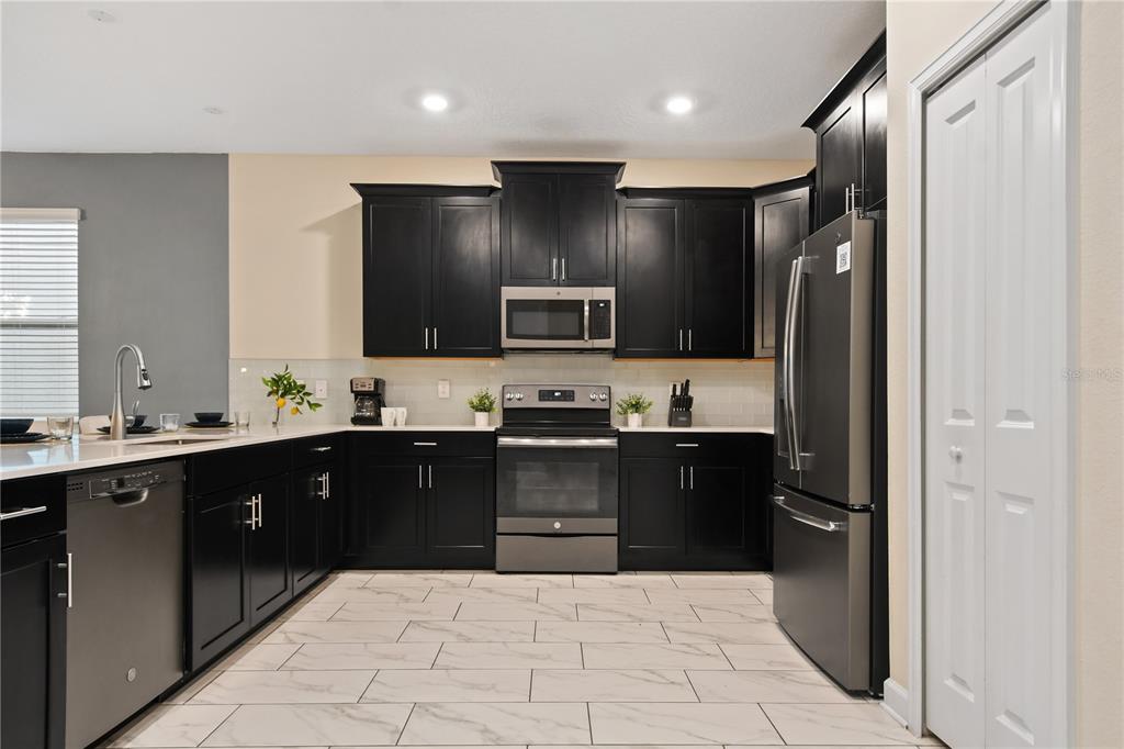 A kitchen features black cabinets, stainless steel appliances, white countertops, and light-colored tiled flooring — 4547 NARRATIVE LANE, KISSIMMEE, FL