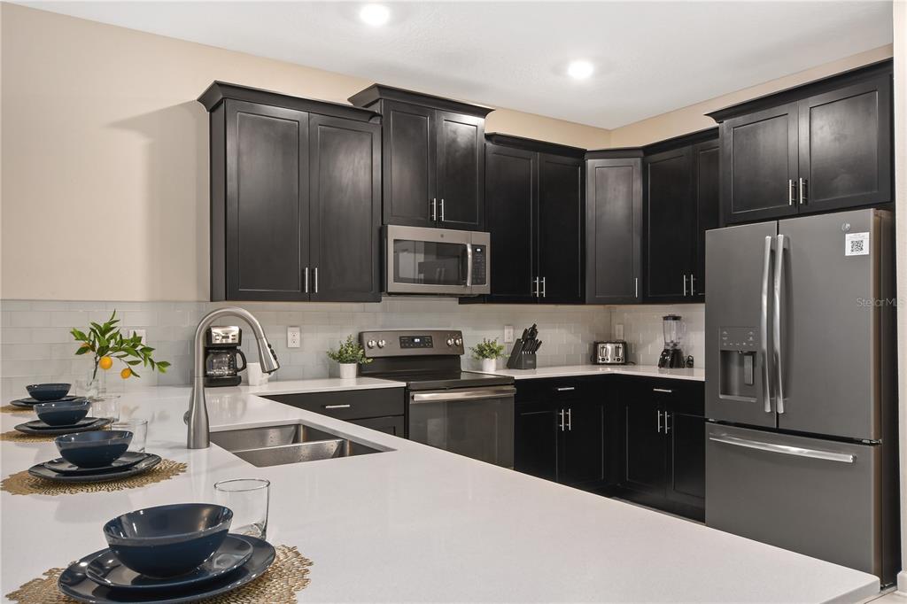 A kitchen features dark cabinets, stainless steel appliances, and a white countertop with a sink — 4547 NARRATIVE LANE, KISSIMMEE, FL
