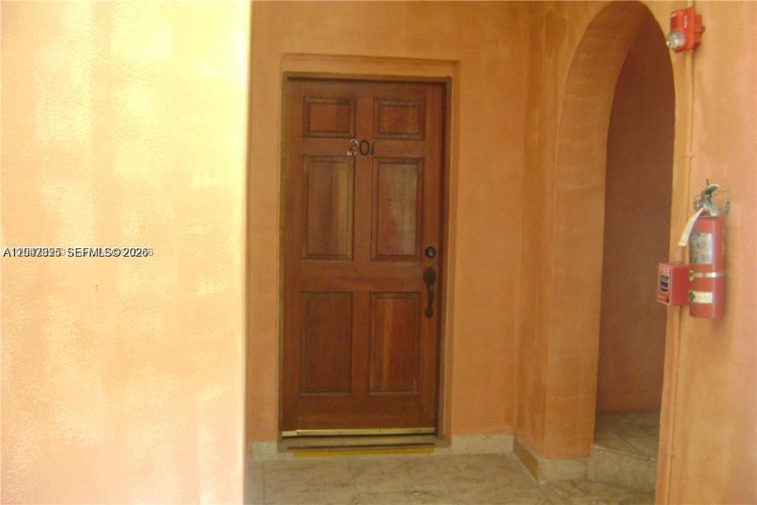 A wooden door with the number 201 is set within an arched, peach-colored stucco entryway — 4812 Pine Tree Dr # 201, Miami Beach FL 33140, MIAMI BEACH, FL