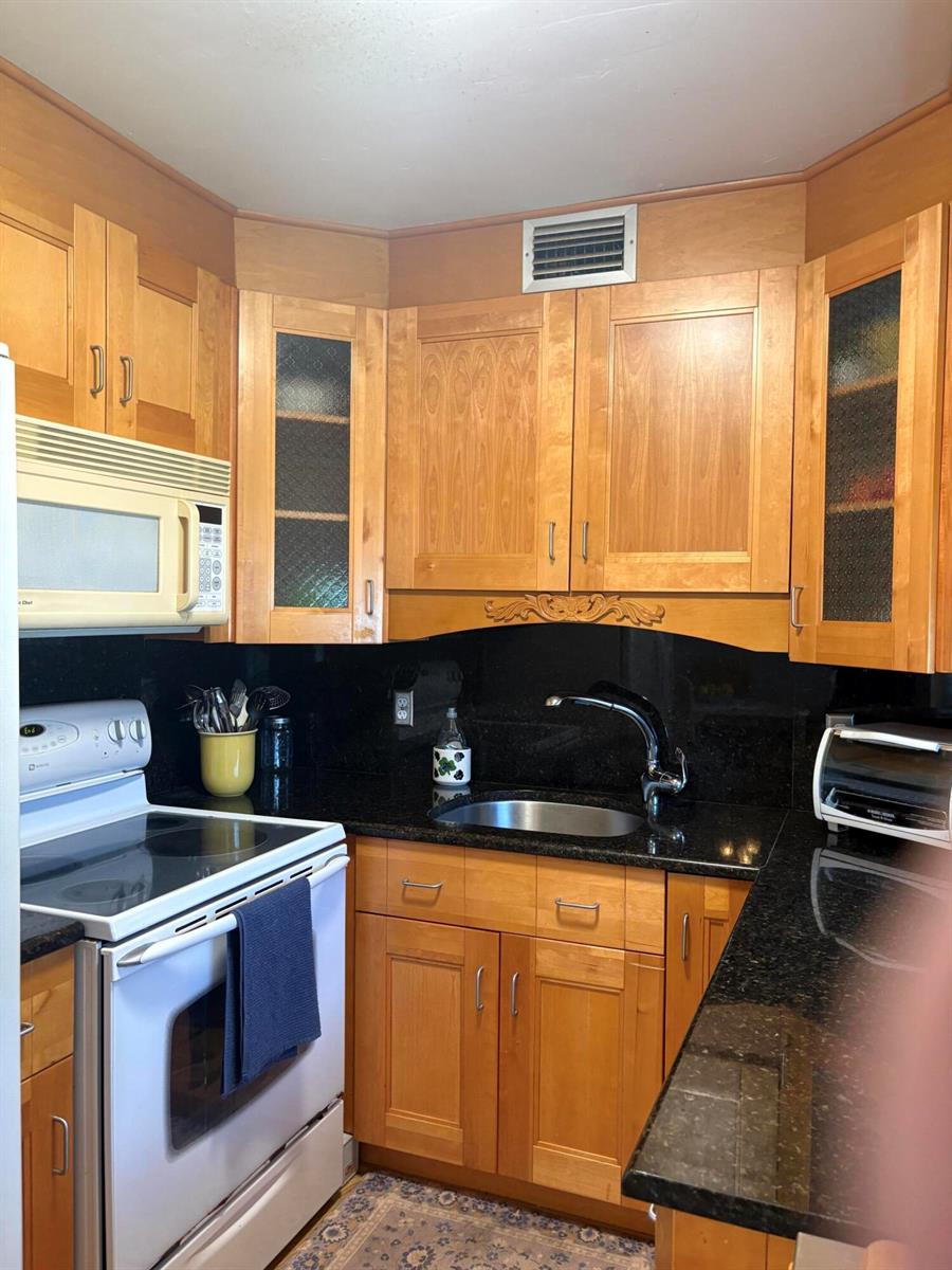 A kitchen features wood cabinets, black granite countertops, a white stove, and a microwave — 25 Kent B, West Palm Beach FL 33417, WEST PALM BEACH, FL