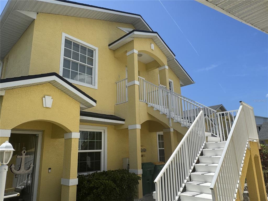 A yellow two-story building features an exterior staircase leading to an upper-level balcony — 169 BOUNDARY BOULEVARD UNIT 169P, ROTONDA WEST, FL