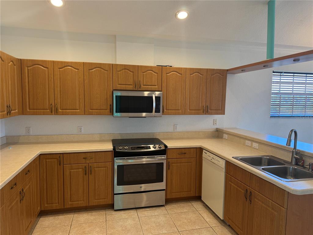 A kitchen features light wood cabinets, beige countertops, and stainless steel appliances — 169 BOUNDARY BOULEVARD UNIT 169P, ROTONDA WEST, FL