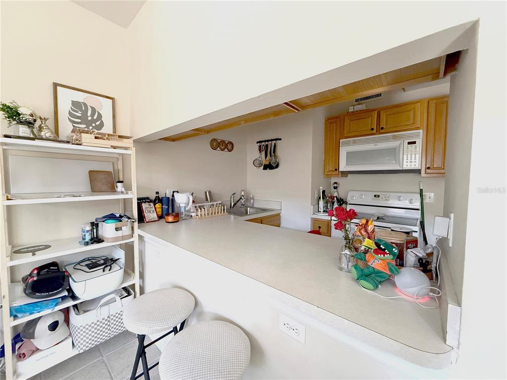 A kitchen with light-colored countertops, wooden cabinets, and a breakfast bar with two stools — 1220 SW 1ST AVENUE UNIT 303, GAINESVILLE, FL