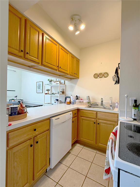 A kitchen features light wood cabinets, white countertops, a white dishwasher, and tiled flooring — 1220 SW 1ST AVENUE UNIT 303, GAINESVILLE, FL