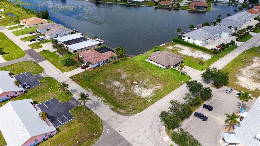 An aerial view shows a vacant residential lot situated between houses near a lake — 304 SW 3RD PLACE, CAPE CORAL, FL