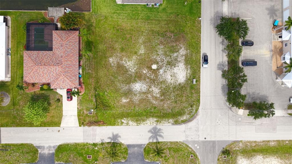 An aerial view shows a vacant residential lot situated between a house and a street — 304 SW 3RD PLACE, CAPE CORAL, FL