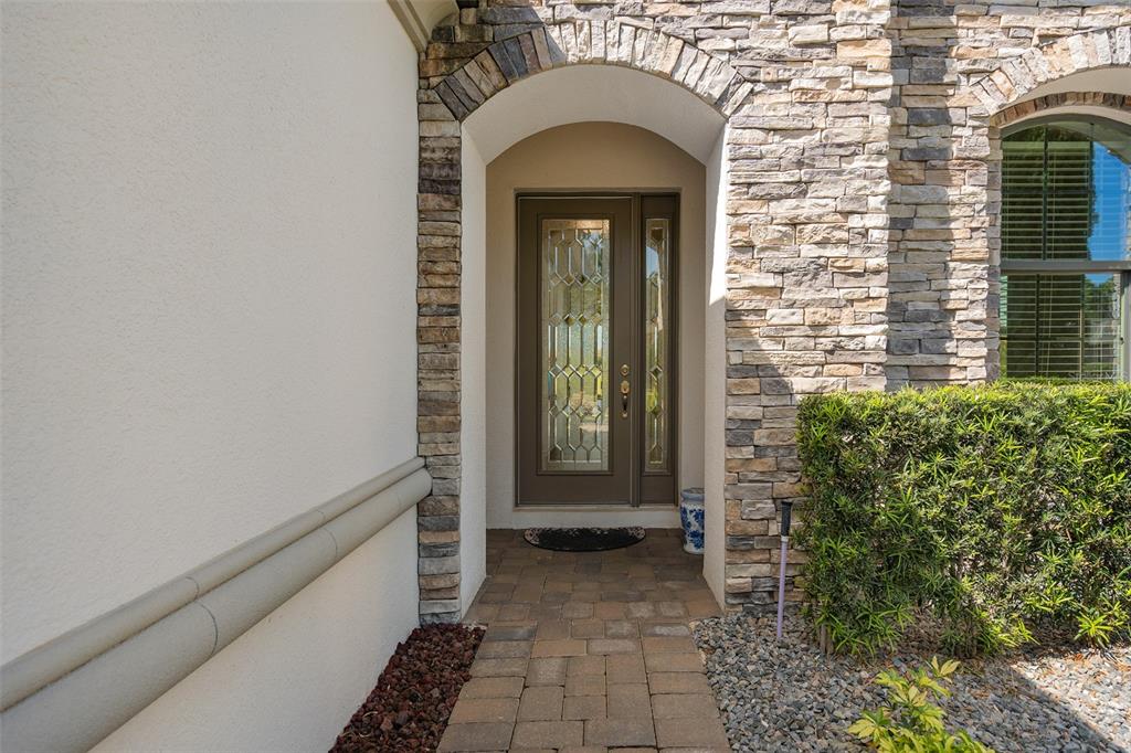 A stone-arched entryway features a brown front door with glass panels and a brick walkway — 1222 ZEEK RIDGE STREET, CLERMONT, FL