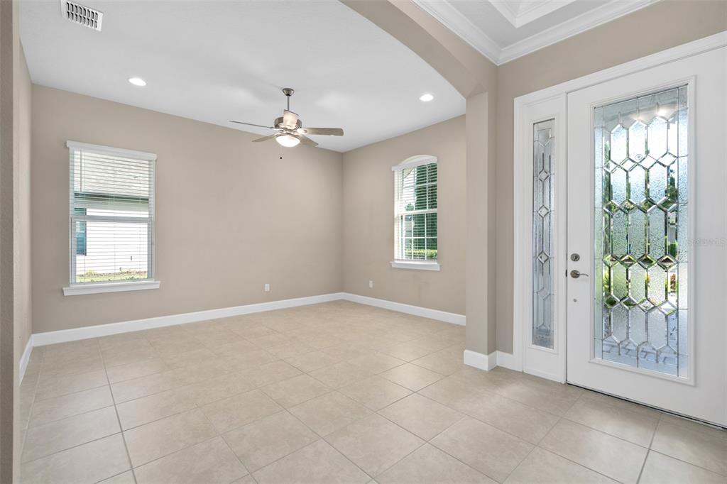 An empty room with beige walls, tile flooring, a ceiling fan, and a glass-paneled front door — 1222 ZEEK RIDGE STREET, CLERMONT, FL